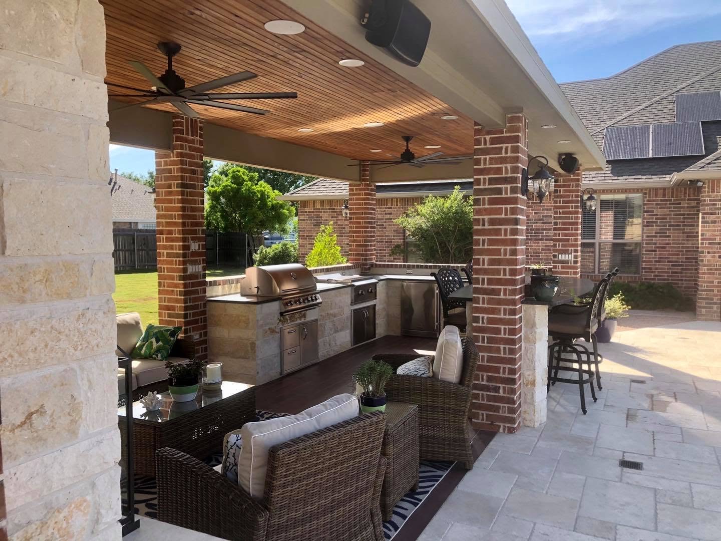 Covered outdoor living space with stone columns, a wood ceiling, and a built-in outdoor kitchen