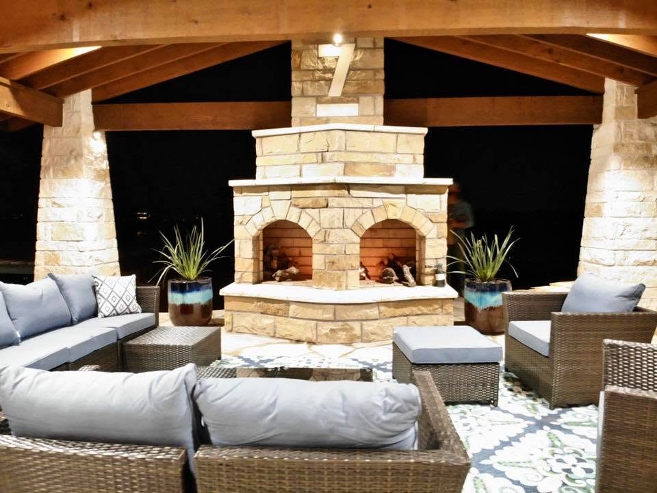 Two-arch stone outdoor fireplace at night under a timber pavilion with lounge seating