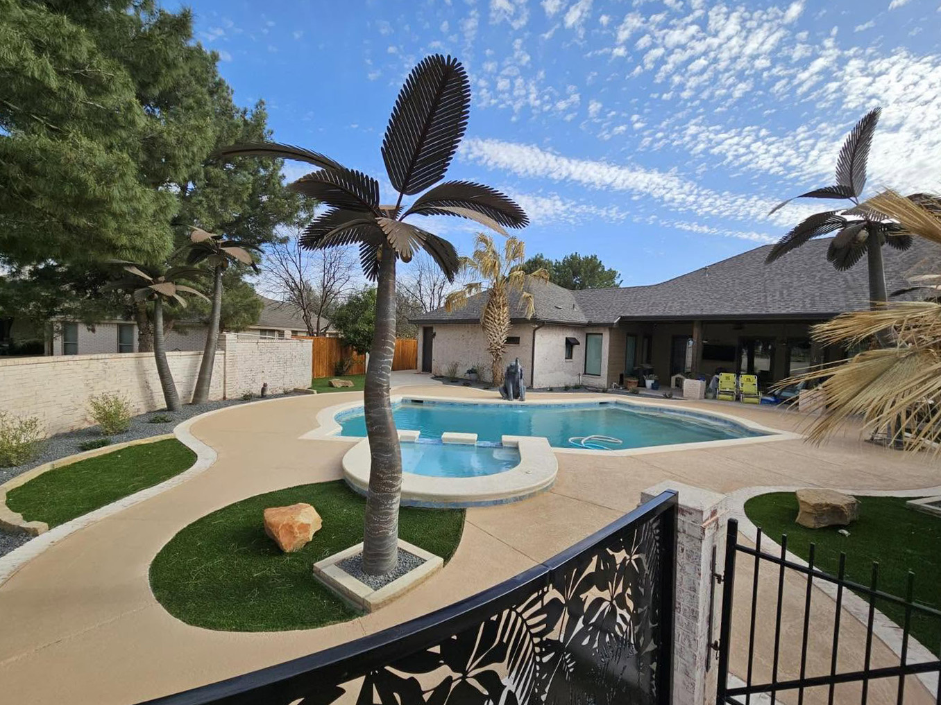 Backyard pool and raised spa with a curved deck, turf islands, and sculpted metal palm trees